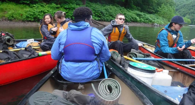 People sit in canoes tethered closely together. 